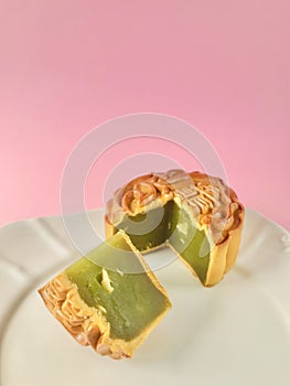 Pandan seeds moon cake with a portion cutout on pink background. vertical.