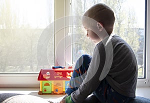 Pandemic isolation - outbreaks of coronovirus, covid-19. The child sadly looks out the window, sitting on windowsill during