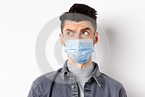 Pandemic lifestyle, healthcare and medicine concept. Confused guy in face mask look left at logo and frowning skeptical