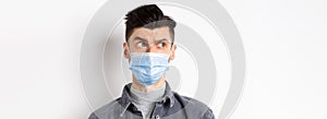 Pandemic lifestyle, healthcare and medicine concept. Confused guy in face mask look left at logo and frowning skeptical