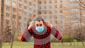 Pandemic, portrait of young frightened student man coughs and hides wearing protective mask so no one sees him outdoor