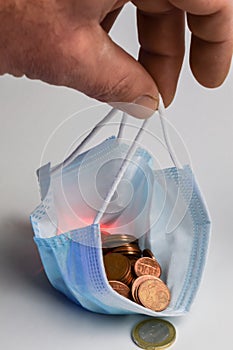 The pandemic purse - Human fingers hold a protective mask full of euro cents, concept to demonstrate the economic impoverishment