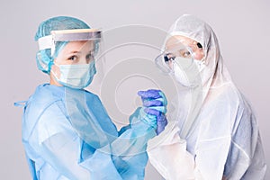 Pandemic. Tired doctors in covid-19 protective gear hold hands in support of a dire situation. Gray background. photo