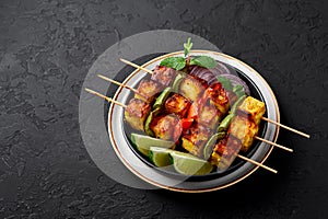 Paneer Tikka at skewers in black bowl at dark slate background. Paneer tikka is an indian cuisine dish. Indian food