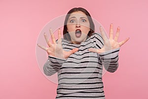 Panic and phobia. Portrait of scared woman in striped sweatshirt raising hands from sudden fear, looking terrified