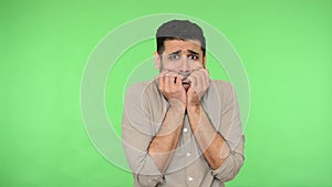 Panicked scared brunette man biting nails to relieve anxiety or stress. green background, chroma key