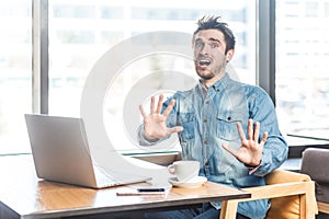 Panicked scared young man working on laptop, showing stop gesture, looks frighten, screaming.