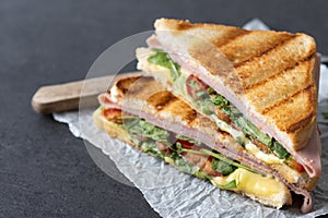 Panini sandwich with ham, cheese, tomato and arugula on black slate background