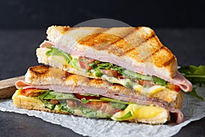 Panini sandwich with ham, cheese, tomato and arugula on black slate background