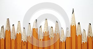 Panning across row of used and worn out yellow pencils with broken pencil tips, with one single and unique sharpened pencil