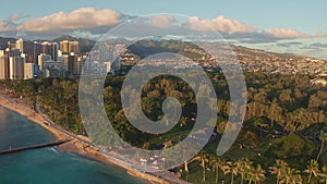 Panning aerial drone slowly flying over a colorful Honolulu Skyline while Sunset in Oahu, Hawaii with Waikiki Beach