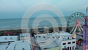 panning aerial footage of the amusement rides at the Carolina Beach Boardwalk with people, hotels, lush green trees