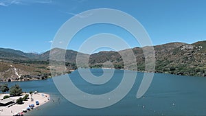 panning aerial footage of the rippling blue waters of Silverwood Lake with a beach and people swimming in the water