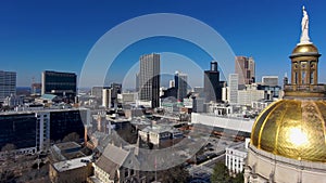 Panning aerial shot of the Georgia Capitol Museum surrounded by skyscrapers and office buildings with cars driving on the freeway