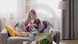 Panning of attractive woman sitting on sofa and knitting at cozy home
