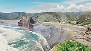 Panning drone video captures stunning aerial view of Piha beach, with distant figures enjoying the sand and surf
