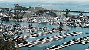 panning footage of the boats and yachts docked in the Dana Point Harbor with vast blue ocean water and lush green trees