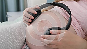 Panning shot of big headphones with playing music on big belly of pregnant woman. Unborn baby listening to classic music