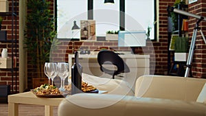 Panning shot of empty cozy apartment living room with appetizer platter and wine bottle on table