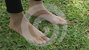 Panning shot of a woman standing barefoot on grass at the park