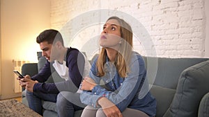 Panning shot young man using social media on mobile phone ignoring his girlfriend at home sofa couch with the woman frustrated