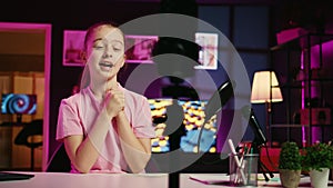 Panning shot of youngster filming video with phone on tripod in pink neon lit living room