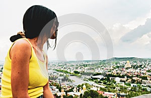 Panning view young caucasian woman stand on viewpoint enjoy scenic Tbilisi city panorama from Narikala fortress in summer. Travel
