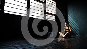 Panning young beautiful woman sitting on floor and wrapping hands with black boxing wraps in club.