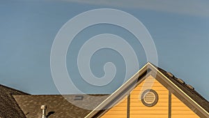 Pano House exterior with roof shingles and round gable window against blue sky