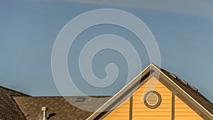 Pano House exterior with roof shingles and round gable window against blue sky photo