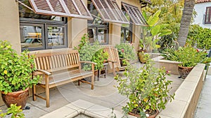 Pano Relaxing patio of house with wooden chair and bench against windows with awning