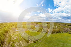 Panorama aerial view of green meadow and field near the path around which are gray and white clouds with a blue sky with a country