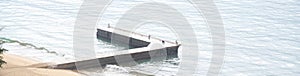 Panorama aerial view L shape concrete fishing pier with beach surf fishermen along sandy shoreline, calm waves at public park in