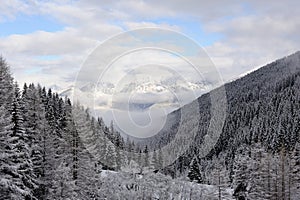 Panorama of Austrian Stubai Alps with mountain ranges and trees covered in snow and blue sky and clouds in winter