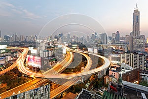 Panorama of Bangkok at dusk with skyscrapers in background and busy traffic on elevated expressways & circular interchanges