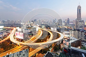 Panorama of Bangkok at dusk with skyscrapers in background and busy traffic on elevated expressways & circular interchanges