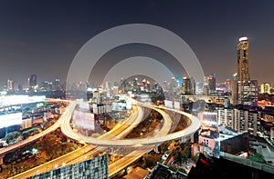 Panorama of Bangkok at dusk with skyscrapers in background and traffic trails on elevated expressways and circular interchanges