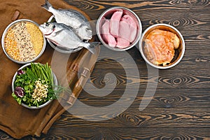 Panorama banner with healthy pet food ingredients in individual bowls on brown wooden background.