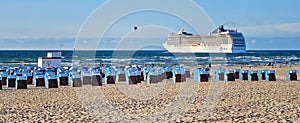 Panorama of a beach with deck chairs and a large cruise ship