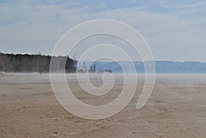 Panorama of a beach in the morning haze against the background of the silhouette of a mountains on the opposite bank of the river.