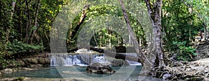 Panorama of a beautiful waterfall with a scrubby beach on the right in the dense forest of Erawan National park in Thailand