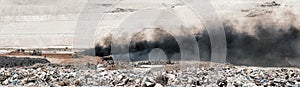 Panorama of black smoke over burning old tyres and piles of garbage at landfill site