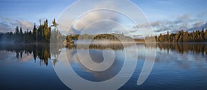 Panorama of blue lake in northern Minnesota with an island and pines on a foggy September morning