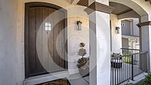 Panorama Brown wood arched front door with glass panes at the facade of home with porch