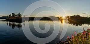 Panorama of a calm lake with small island and golden sunset evening light on the trees and forest on the lakeshore in the