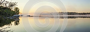 Panorama of a calm northern Minnesota lake and fog at dawn during spring with docks along the shoreline