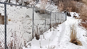 Panorama Chain link fence with barbed wires on snow covered hill slope viewed in winter