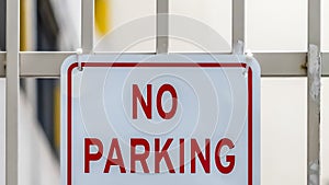 Panorama Close up of No Parking sign on awhite metal gate with building in the background