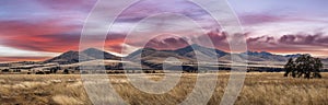 Panorama of a distant mountain range with hills covered in grass in the forground with a dramatic sunset