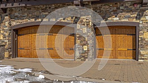 Panorama facade of home featuring two hinged wooden garage doors and stone brick wall